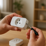 hands holding a smart plug near an outlet with tools on table